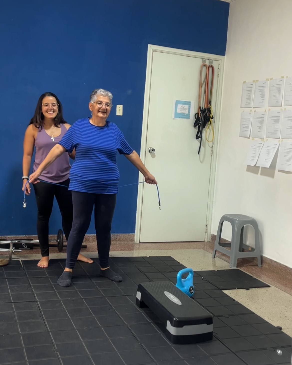 Atleta senior sonriendo durante un ejercicio con banda elástica, acompañada por Andrea